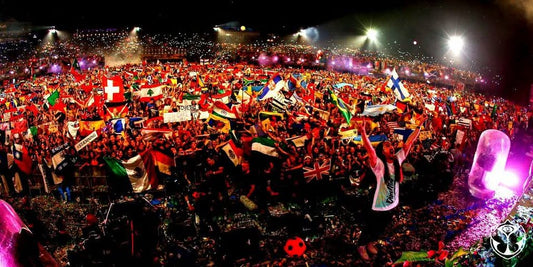 “Wide night-time shot of a packed outdoor concert crowd waving Lebanese and international flags under bright stage lights.”  “صورة بانورامية لحشد جماهيري كثيف في حفل موسيقي ليلي بالهواء الطلق يلوّح بالأعلام اللبنانية والدولية تحت أضواء المسرح.